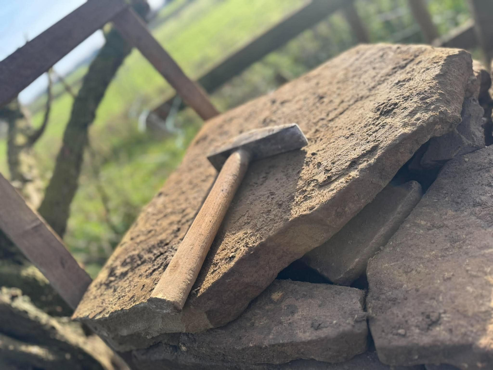 Sandstone coping stones laid on a wall under construction with a mason's hammer alongside