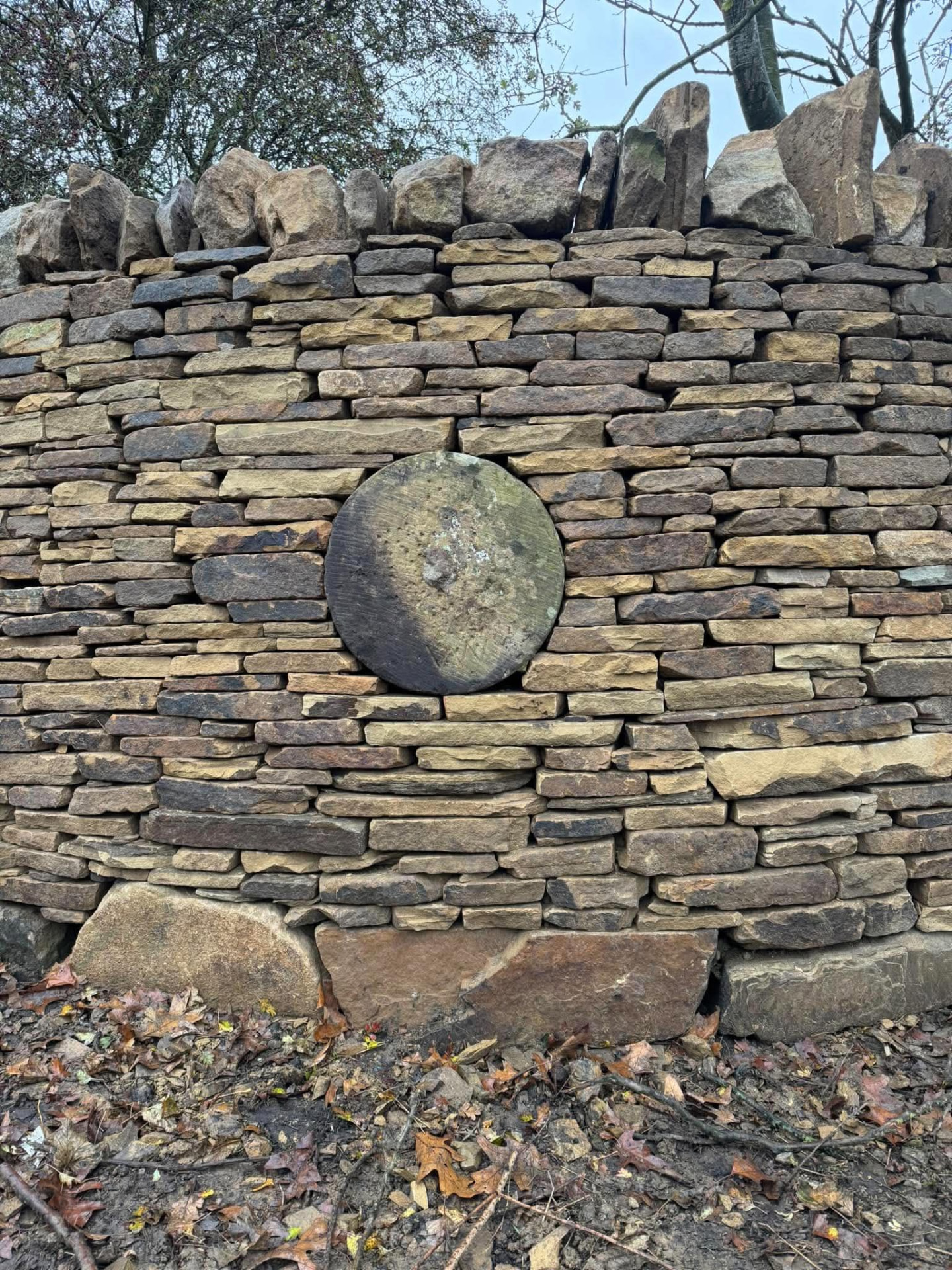 Dry stone boundary wall with a stone roundel set into a wooded setting