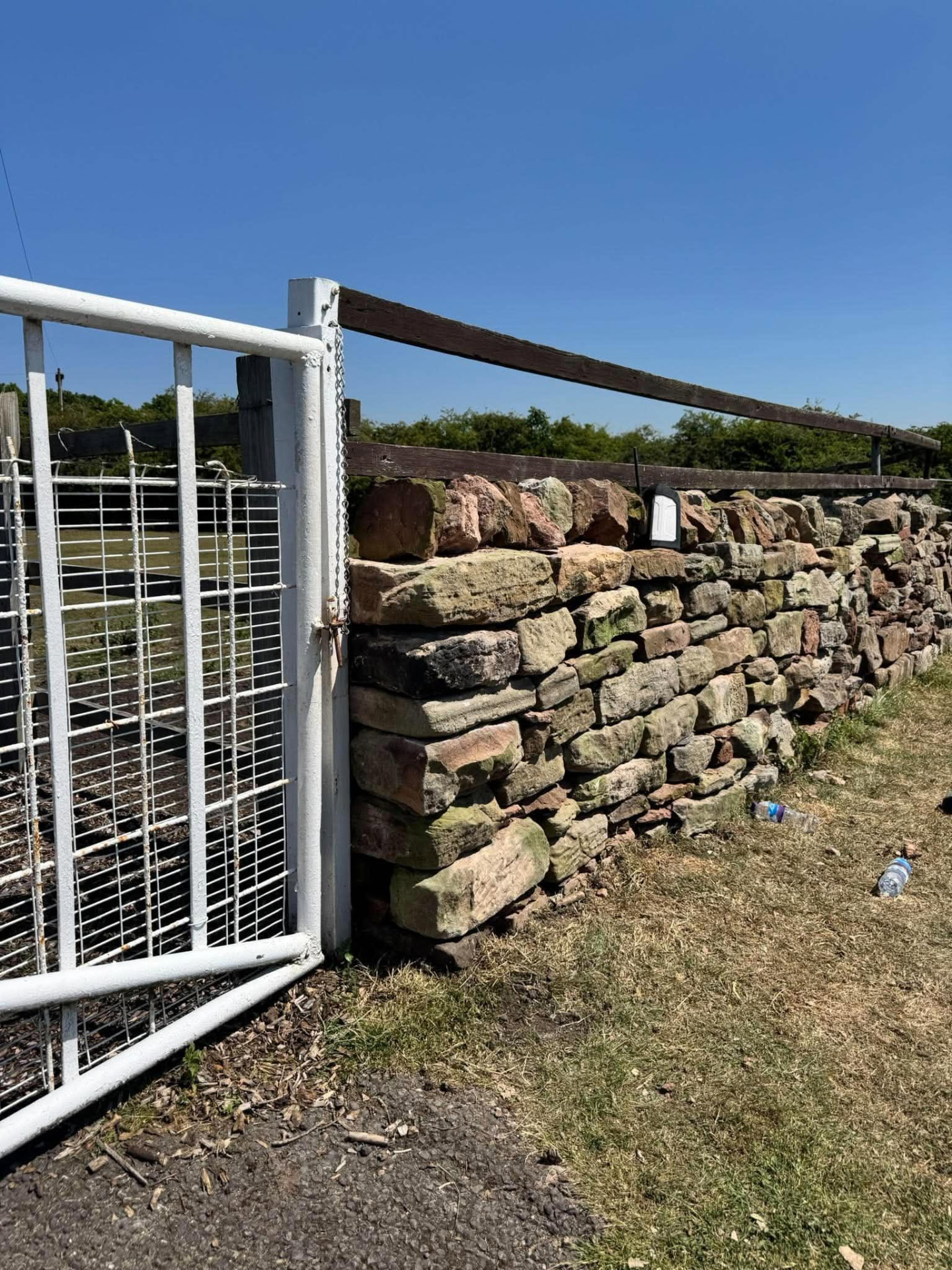 Weathered field boundary wall built alongside a fence with a white metal gate